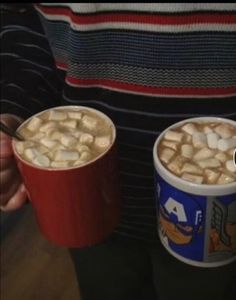 two cups of hot chocolate with marshmallows in them are being held by someone