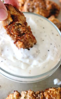 a person dipping something into a small glass bowl filled with ranch dressing and fried chicken wings