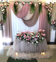 a table with flowers and candles on it in front of a curtained area for an event