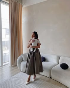 a woman holding a baby in her arms while standing next to a couch and window