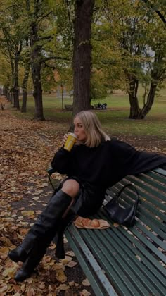 a woman sitting on top of a bench next to a forest filled with lots of leaves