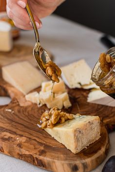 a person is spooning cheese from a wooden cutting board with other cheeses on it