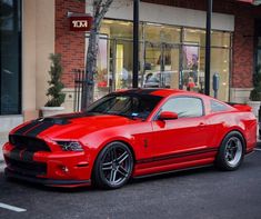 a red mustang parked in front of a building