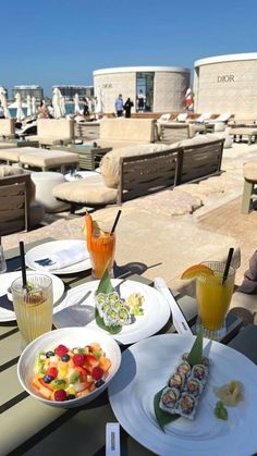 there are plates with food on them and drinks in front of the water at this beachside restaurant