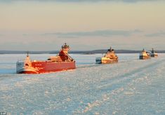 several large boats floating on top of a frozen lake next to shore covered in snow