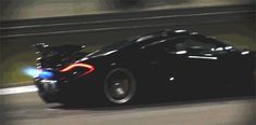 a black sports car driving down the road with its lights on in front of it