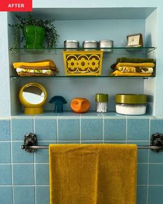 a blue tiled bathroom with yellow towels hanging on the wall and green plants in the corner