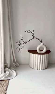 a white vase sitting on top of a wooden table next to a curtained window