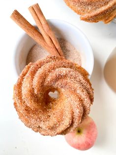 cinnamon sugar doughnuts and apples on a white surface with cinnamon sticks in the bowl