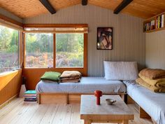 a room with two beds and a table in it, next to a window that looks out onto the woods