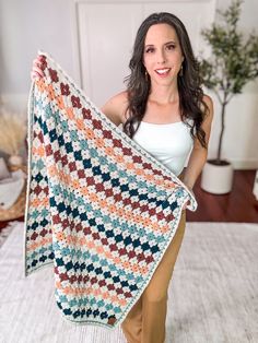 a woman is holding up a crocheted blanket