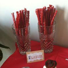 two glass vases filled with red candy sticks on top of a red table cloth