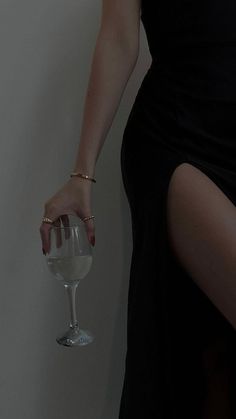 a woman in a black dress holding a wine glass with her right hand on the wall