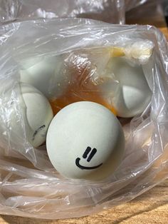 three eggs with faces drawn on them sitting in a plastic wrapper next to an orange