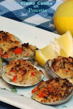 clams with pancetta served on a white plate next to lemon wedges