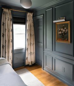 an empty bedroom with blue walls and wood flooring is pictured in this image, there are curtains on either side of the bed