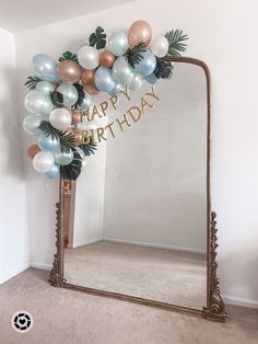 a birthday arch with balloons and palm leaves on it in front of a mirror that says happy birthday