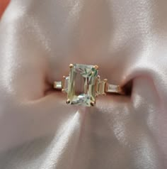 an emerald cut ring with three baguettes on it's side, sitting on a white satin surface