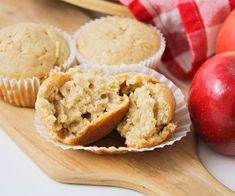 an apple muffin cut in half on a wooden cutting board next to some apples