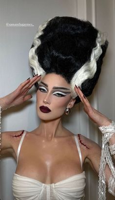 a woman with black hair and white makeup is posing in front of a wall wearing an elaborate wig