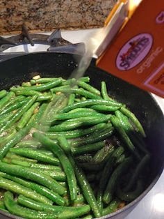 green beans are being cooked in a pan on the stove top next to a cookbook