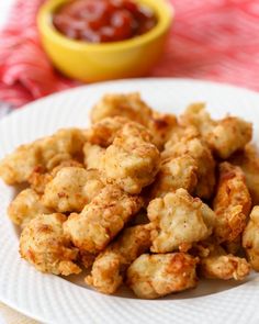 some fried food on a white plate next to a bowl of ketchup