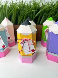 several colorful boxes with writing paper attached to them sitting on a table next to some grass