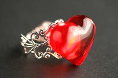 "A fun Valentine themed ring designed with a bright red puffy acrylic heart that has been set upon an adjustable filigree ring base in your choice of finish in this handmade that's adjustable from size 6 and up. Heart Size: 23mm w x 19mm h This handmade ring is adjustable from size 6 and up, making it comfortable no matter the size of the wearer's fingers as well as ideal for switching from finger to finger depending on mood or preference. With a bit of altering to the band, this ring can be mad Cute Red Ring As Gift, Cute Red Ring For Gift, Adjustable Red Heart Ring As Gift, Red Adjustable Heart Ring For Valentine's Day, Adjustable Red Heart Ring For Valentine's Day, Valentine's Day Red Heart Ring, Red Resin Rings As A Gift, Red Resin Rings Suitable For Gifts, Red Resin Ring Suitable For Gifts