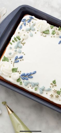 a cake with white frosting and blue flowers is on a baking sheet next to a knife