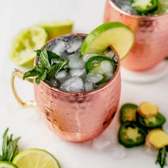 two copper mugs filled with ice, lime and mint garnish on a white surface