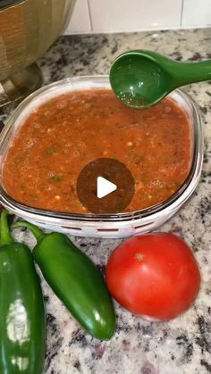 some green peppers and tomatoes are on the counter next to a bowl of chili sauce