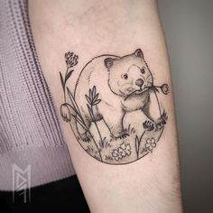 a black and white bear tattoo on the right arm with daisies around its neck