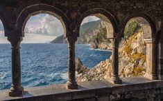 an old stone building with arches overlooking the ocean and rocky cliffs in the distance