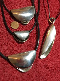 three silver necklaces on a red surface with a penny in the middle and two black leather cords