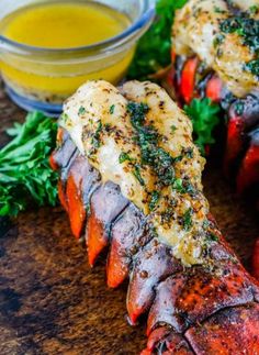 grilled lobsters on a wooden cutting board with mustard and parsley next to them