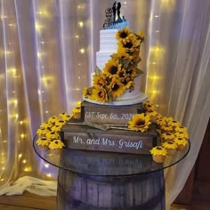 a wedding cake with sunflowers on top sits in front of a wine barrel