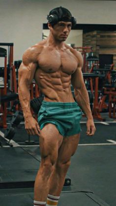 a man with no shirt and green shorts standing in front of a gym equipment area