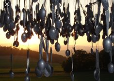 metal spoons hanging from the ceiling in front of a sunset with trees and grass