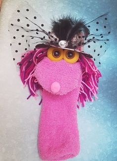 a pink stuffed animal wearing a hat with feathers on it's head and eyes