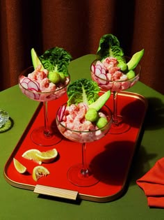 two glasses filled with shrimp and lettuce on top of a red serving tray