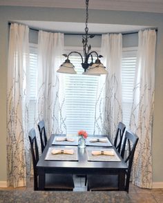 a dinning room table with place settings in front of the window and two lights hanging from the ceiling