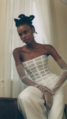 a woman sitting on top of a wooden bench wearing white gloves and a dress with sheer sleeves