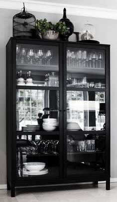 a black china cabinet with glass doors and dishes on top