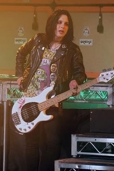 a man with long hair playing a bass guitar in front of other guitars and amps