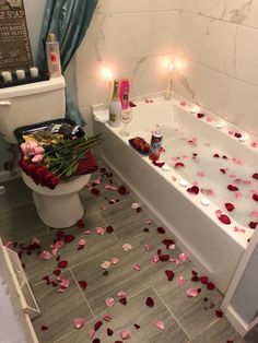 a bathtub with rose petals on the floor next to a toilet and candles in it