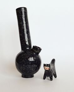 a black vase with a cat figurine next to it on a white surface