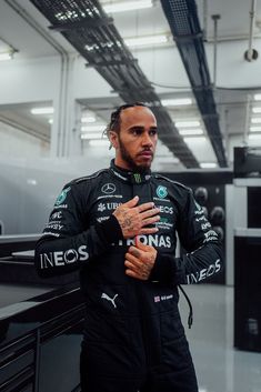 a man in a racing suit standing next to a black car with his hands on his chest