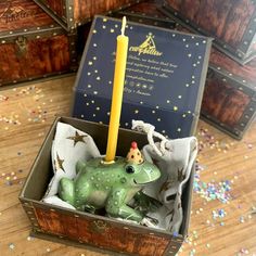 a green frog figurine in a box with a candle