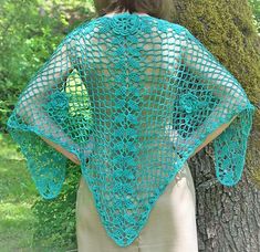 a woman standing next to a tree wearing a blue crocheted shawl