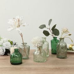 several green glass vases with flowers in them